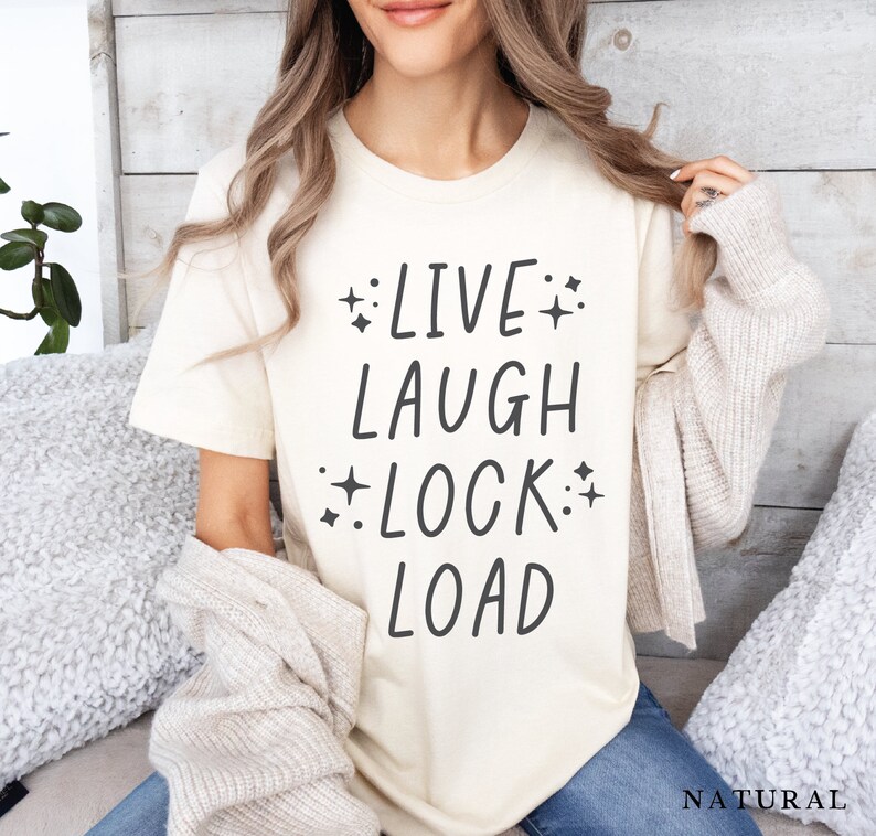 May include: A cream colored t-shirt with the text "LIVE LAUGH LOCK LOAD" in black lettering with small stars around the words.