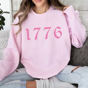 May include: Pink sweatshirt with the number 1776 printed in a pink gothic font.