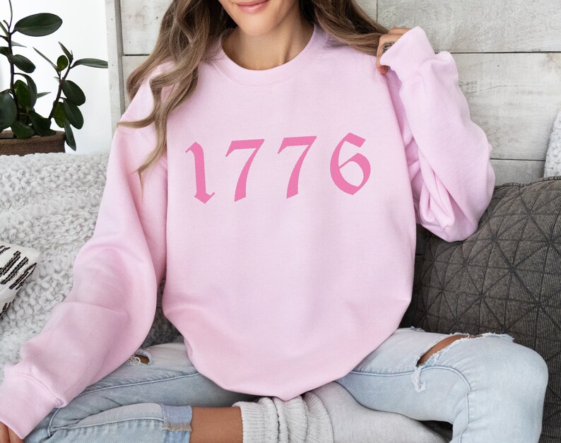 May include: Pink sweatshirt with the number 1776 printed in a pink gothic font.
