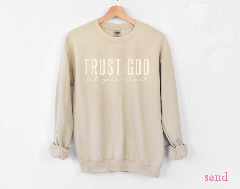 以下が含まれることがあります： サンドカラーのトレーナーに「TRUST GOD not your government」という白い文字がプリントされています。