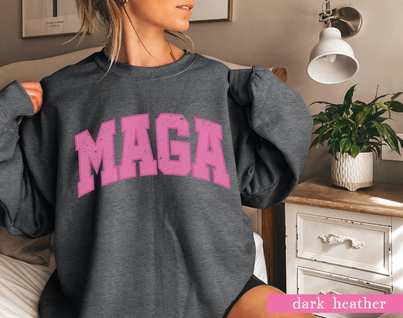 May include: A dark heather grey sweatshirt with the word "MAGA" printed in pink on the front.