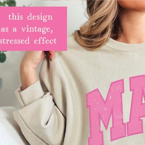May include: A light beige sweatshirt with a pink vintage-style graphic that says "MA" with a distressed effect. The design has a vintage, distressed effect.