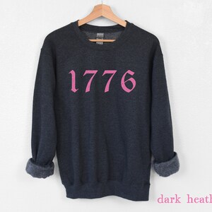 May include: Dark heather grey sweatshirt with the number 1776 printed in pink.