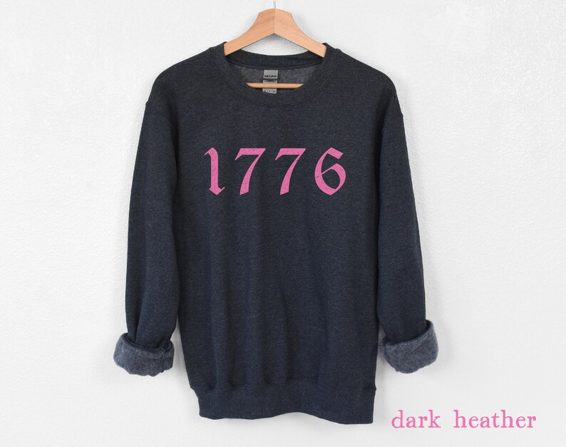 May include: Dark heather grey sweatshirt with the number 1776 printed in pink.
