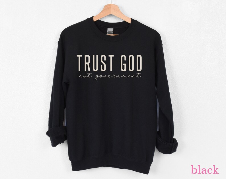 以下が含まれることがあります： 白い文字で「TRUST GOD not government」と書かれた黒いスウェットシャツ