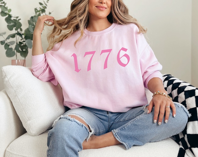 May include: A pink sweatshirt with the number 1776 printed in a pink gothic font.