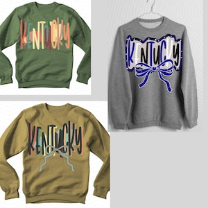 May include: Three sweatshirts with the word "Kentucky" in various designs. One is olive green with colorful text, another is gray with a blue bow and text, and the third is tan with a bow and text.