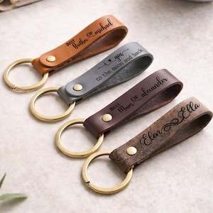 May include: Four leather keychains with gold-tone metal rings and rivets. The tan keychain reads 'BEST Brother OF michael', the grey one 'I love you to the moon and back', the dark brown one 'BEST Mum OF alexander', and the textured brown one 'Elen infinity Ella'.