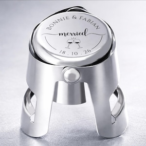 May include: A silver-coloured metal champagne bottle stopper with a circular top engraved with the text BONNIE & FABIAN, the word merried, an illustration of two clinking wine glasses, and the date 18. 10. 26 centred on the flat surface.