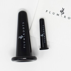 May include: Two black glass facial suction cups with the text "PLUM ROOTS" and a small leaf design printed on them.