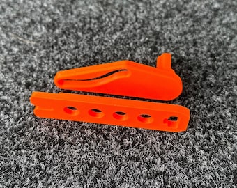 May include: Orange plastic toy with a long, curved top and a flat base with five holes. The toy is on a gray carpet.