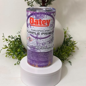 May include: A purple tumbler featuring the "Oatey" logo and the words "FOR CPVC, PVC PURPLE PRIMER". The tumbler is cylindrical and has a metallic sheen. The product is displayed on a white pedestal with greenery and berries in the background.
