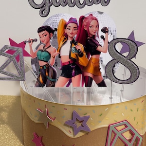 May include: A birthday cake topper featuring three animated female singers with microphones. The topper includes the name "Giulia" and the number "8" in silver glitter. The cake is decorated with star and diamond shapes.