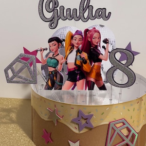 May include: A custom cake topper featuring three animated female figures with microphones, the name "Giulia", and the number "8". The cake is decorated with star and diamond shapes, and has a brown and tan frosting design.