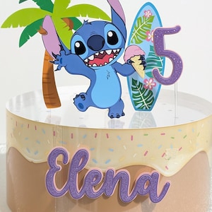 May include: A cake with a cartoon character, palm tree, surfboard, and the number 5. The cake has a light brown and beige frosting with sprinkles and the name "Elena" in purple script.