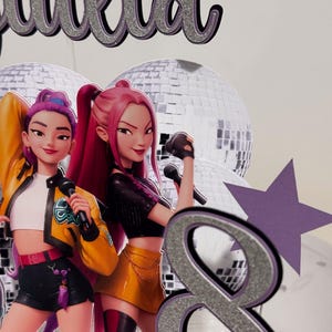 May include: A cake topper featuring two animated female singers with microphones, a silver glitter number 8, and the name "Julia" in silver glitter. The singers are in colorful outfits, with disco balls in the background.