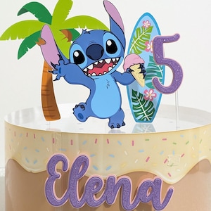 May include: A cake topper featuring the character Stitch, a surfboard, a palm tree, and the number 5. The cake is decorated with the name "Elena" and sprinkles. The cake is designed for a birthday celebration.