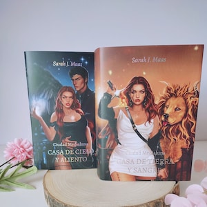 Op de afbeelding: Twee paperback boeken met kleurrijke omslagen waarop een vrouw met rood haar en een leeuw te zien zijn. De titels van de boeken zijn "Casa de Cielo y Aliento" en "Casa de Tierra y Sangre".