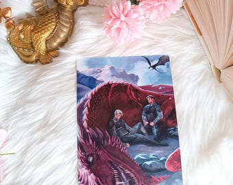 May include: A print featuring two figures in a snowy landscape with a large red dragon. The figures are wearing dark clothing and are standing near the dragon's head. The dragon's wings are spread out behind it.