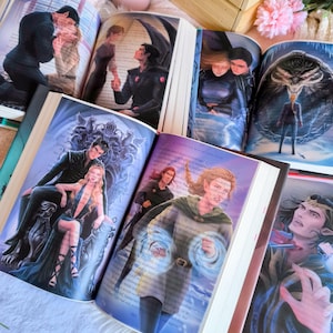 Puede incluir: Libros abiertos con ilustraciones de fantasía. Las páginas muestran obras de arte coloridas de personajes en varias escenas. Los libros están abiertos, revelando dibujos detallados de personas y criaturas, con un enfoque en temas de fantasía.