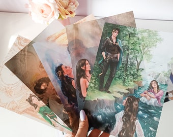 May include: A hand holds a fan of fantasy art prints. The prints feature illustrations of characters in various settings, including a forest, a body of water, and a celestial background. The art style is detailed and colorful, with a focus on character design.