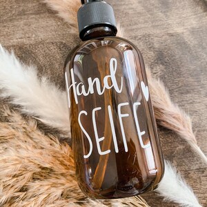 Könnte beinhalten: Eine braune Glasflasche mit einer Pumpspender und einem weißen Etikett, auf dem "Hand Seife" mit einem kleinen Herzen steht.