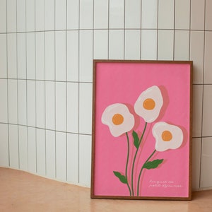 May include: A framed pink print with three white fried egg illustrations on stems with green leaves. The text "hungry as hell, darling" is at the bottom of the print.
