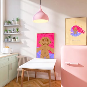 Op de afbeelding: Een roze keuken met een witte tafel en stoelen, een roze koelkast en twee ingelijste prints van een cartoon-troll met roze haar. De tekst op een print luidt "The Birth of a Friend".
