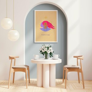 Op de afbeelding: Een gouden ingelijste print met een gele achtergrond en een paarse en roze illustratie van een baby in een schelp. De tekst "The Birth of Venus" staat onder de illustratie.