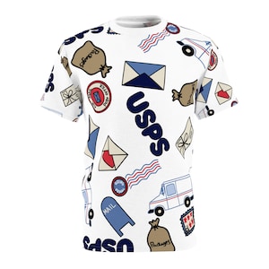 May include: White t-shirt with a blue, red, and white USPS themed pattern. The pattern includes mailboxes, mail trucks, envelopes, and the USPS logo.