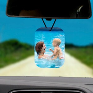 May include: A car air freshener with a photo of a woman and a child playing in a swimming pool. The photo is printed on a white background.