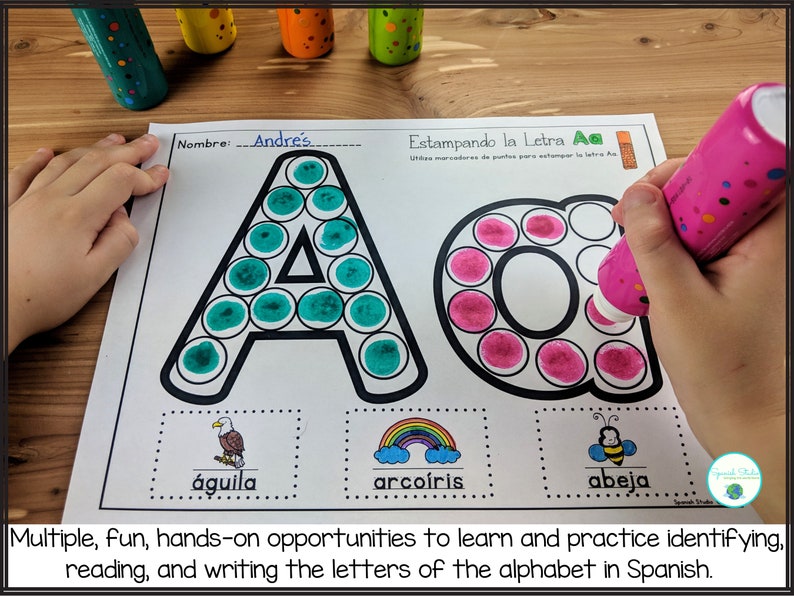 May include: A Spanish alphabet learning worksheet with the letter 'A' outlined in black and filled in with green and pink dot stickers. The worksheet also includes the words 'aguila', 'arcoiris', and 'abeja' with illustrations of an eagle, a rainbow, and a bee.
