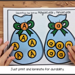 May include: A printable worksheet with two blue bags, one with the letter "A" in uppercase and the other with the letter "a" in lowercase. The bags are filled with yellow circles, each containing a letter "A" or "a". The text "Identifico las letras May&uacute;sculas y Min&uacute;sculas" is at the top of the worksheet. The text "Just print and laminate for durability." is at the bottom of the worksheet.