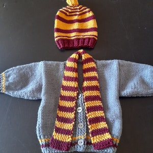May include: A grey knitted cardigan with a burgundy and gold striped scarf and matching hat.