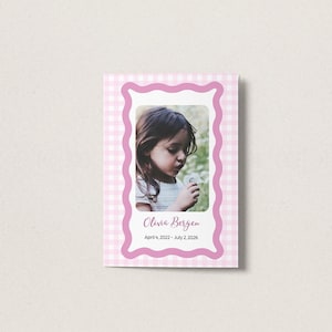 Puede incluir: Una tarjeta rectangular con un borde de cuadros vichy en rosa claro y blanco. Un marco central de bordes ondulados contiene la fotografía de un niño. El texto dice Olivia Bergen y las fechas 4 de abril de 2022 - 2 de julio de 2026.