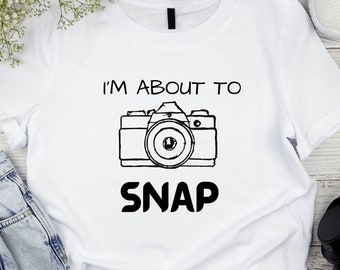 May include: White t-shirt with a black graphic of a camera and the text "I'm about to snap".