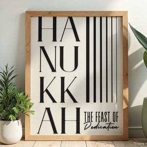 May include: Wooden framed art print with the word "HANUKKAH" in large black letters, with vertical black stripes on the right. The text "THE FEAST OF DEDICATION" is below. The print is displayed with potted plants.