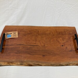 May include: A large, rectangular wooden serving tray with live edge details. The tray has two black metal handles and a small tag that reads "Handcrafted Wood Creations, Tray with Handles, Made in USA".