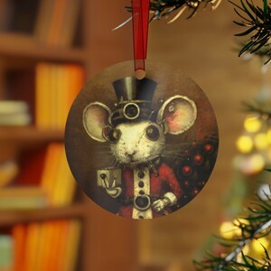 May include: A round, brown, Christmas ornament featuring a white mouse wearing a red and black steampunk outfit and a top hat. The mouse is holding a small cup and has a pipe in its mouth. The ornament is hanging from a red ribbon on a Christmas tree.