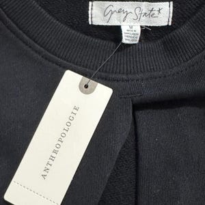 May include: A black sweatshirt with a white tag that says "Grey State" and a white tag that says "Anthropologie".