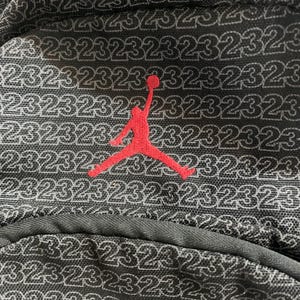 K&ouml;nnte beinhalten: Schwarzer Rucksack mit einem roten gestickten Basketballspieler-Logo und der Zahl 23, die sich in einem Muster auf dem Stoff wiederholt.