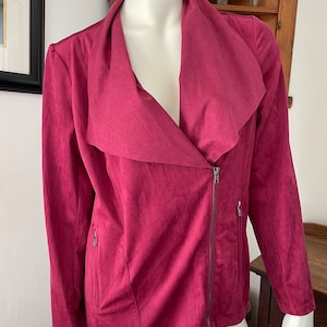 May include: A burgundy faux suede jacket with a long, draped collar and a zipper closure. The jacket has two zippered pockets on the sides.