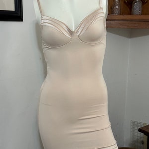 May include: A nude-colored body shaper with a smooth, seamless design. The shaper has adjustable straps and a low back. It features a satin-like trim around the neckline and hem.