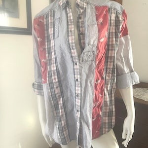 Pode incluir: Uma camisa de manga comprida com bot&otilde;es e design de patchwork. A camisa &eacute; feita de uma variedade de tecidos, incluindo xadrez, listras e cores s&oacute;lidas. A camisa tem um esquema de cores vermelho, branco e azul.