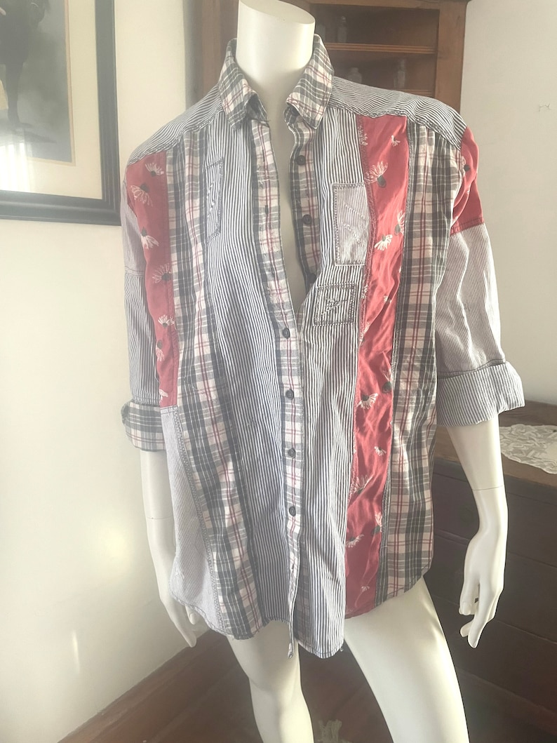 Pode incluir: Uma camisa de manga comprida com bot&otilde;es e design de patchwork. A camisa &eacute; feita de uma variedade de tecidos, incluindo xadrez, listras e cores s&oacute;lidas. A camisa tem um esquema de cores vermelho, branco e azul.