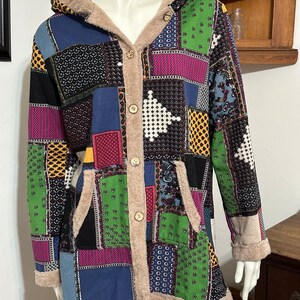 May include: A long-sleeved patchwork hooded jacket with a button-up front. The jacket is made of a variety of fabrics in different colors and patterns, including green, blue, pink, yellow, and black. The jacket has a faux fur lining and a hood with a drawstring.