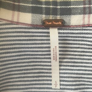 Pode incluir: Uma camisa listrada em preto e branco com uma etiqueta Free People. A etiqueta &eacute; marrom com texto branco e diz "Free People". A etiqueta tamb&eacute;m diz "Made in China" e "Fabriqu&eacute; en Chine".