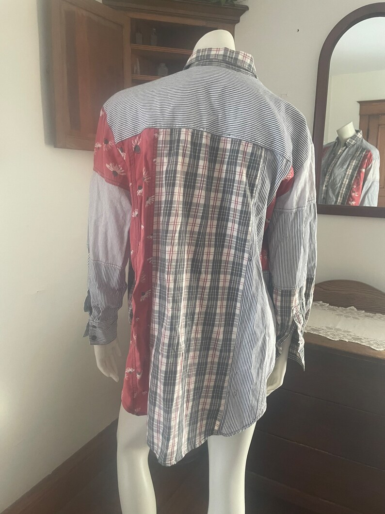 Pode incluir: Uma camisa de manga comprida feita de tecido patchwork. A camisa &eacute; azul, branca, vermelha e preta com um padr&atilde;o floral. A camisa est&aacute; em um manequim.