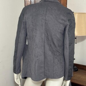 Pu&ograve; includere: Un blazer grigio scuro con un aspetto strutturato simile alla pelle scamosciata. La giacca ha maniche lunghe e un colletto classico. La vista posteriore del blazer &egrave; mostrata su un manichino.