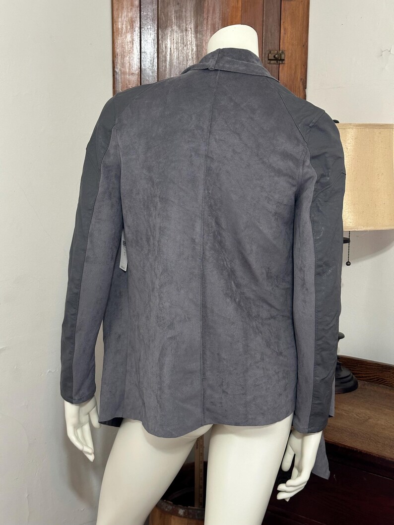 Pu&ograve; includere: Un blazer grigio scuro con un aspetto strutturato simile alla pelle scamosciata. La giacca ha maniche lunghe e un colletto classico. La vista posteriore del blazer &egrave; mostrata su un manichino.